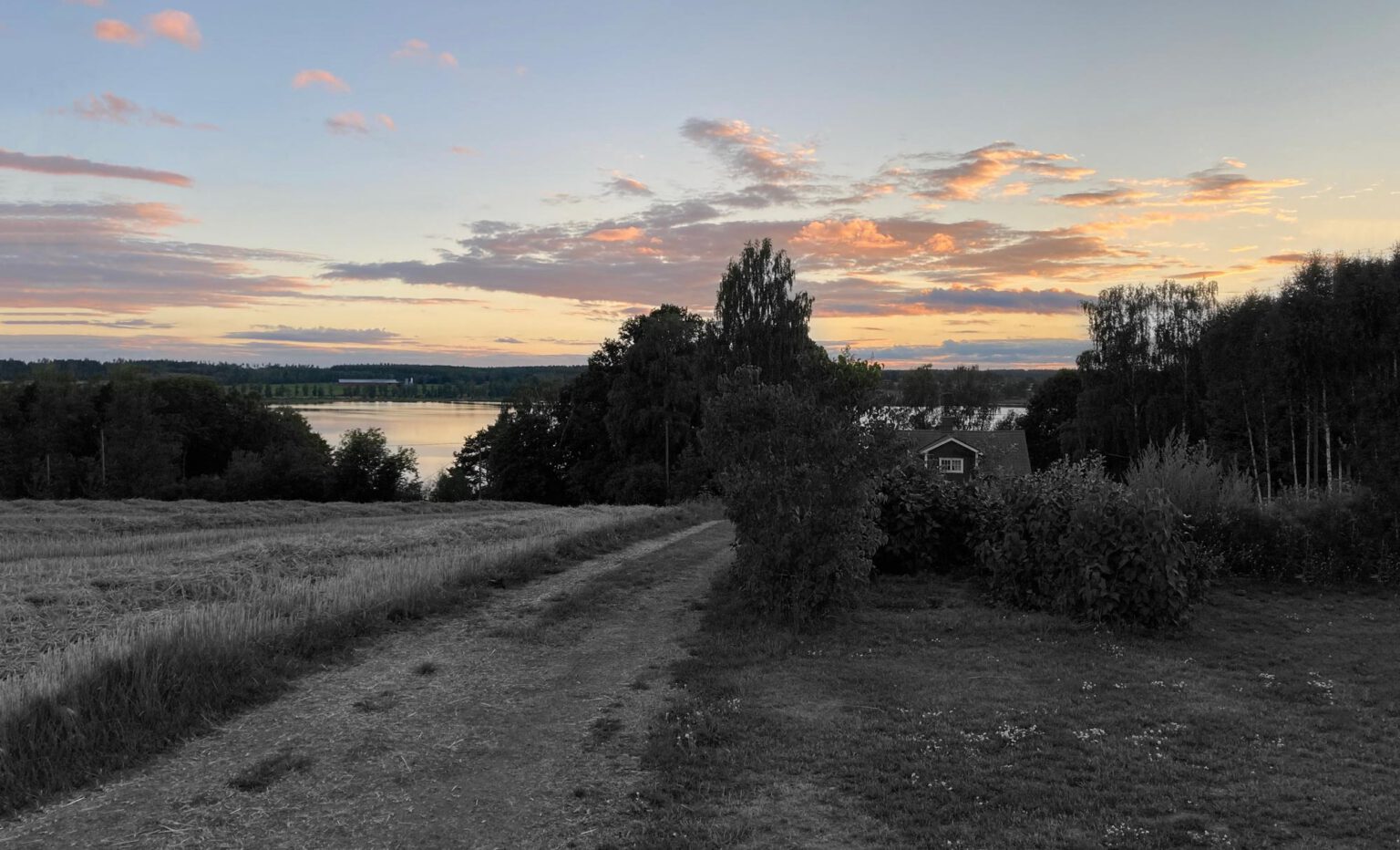 Sonnenuntergang in Schweden. Kleines Haus am See, von Wiesen und Bäumen umgeben.